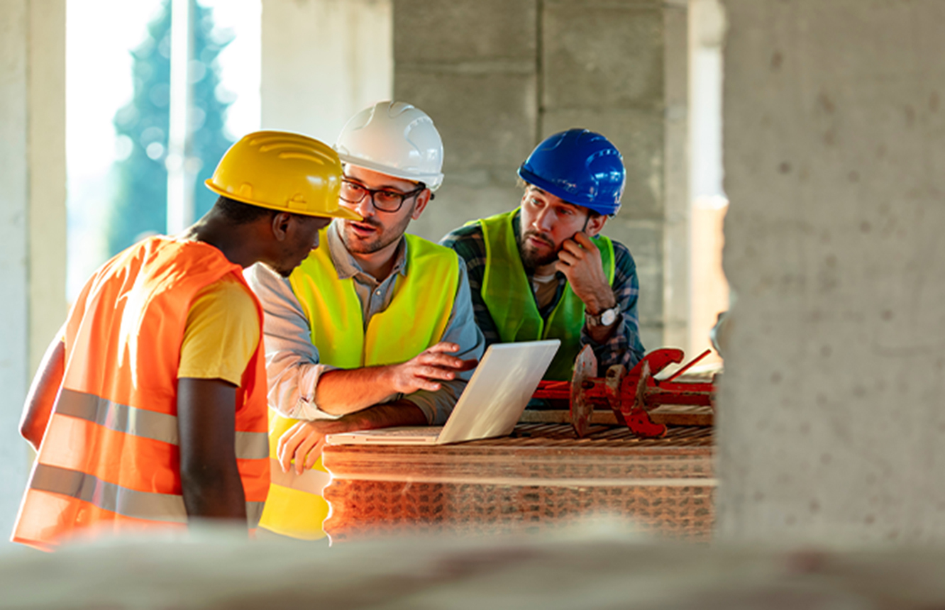 Workers in hard hats discussing over a laptop